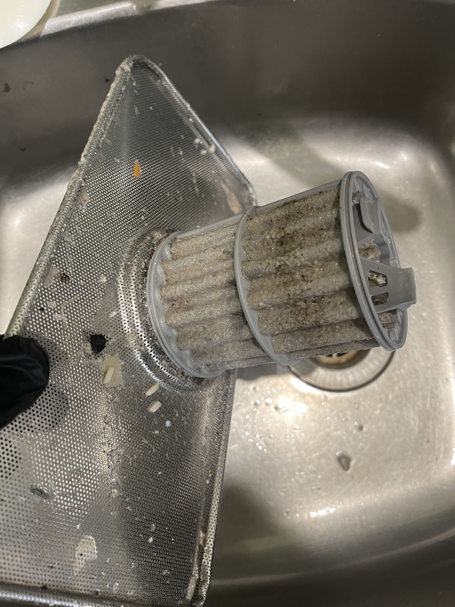 A dishwasher drain pump filter before cleaning, visibly blocked with food debris.